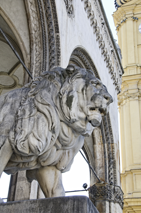 Bild: Löwe in der Feldherrnhalle zu München vor der Theatinerkirche. Dieser Löwe hat sein Maul weitgehend geschlossen. Sein Pendant auf der Seite der Residenz hat das Maul geöffnet. Es gibt dazu eine Legende: Wir können und sollen gegenüber der staatlichen Macht das Maul aufreissen und uns selbstverständlich wehren, die christliche Tradition unseres Vaterlandes soll aber nicht in Frage gestellt werden.