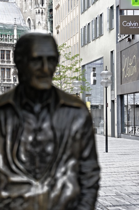 Bild: Fußgängerzone Rosenstraße in München mit Edelboutiquen. Obdachloser vor Nobelboutiquen. NIKON D700 mit AF-S NIKKOR 28-300 mm 1:3,5-5,6G ED VR ¦¦ ISO800 ¦ f/5.0 ¦ 1/60 s ¦ FX 112 mm.