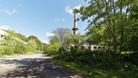 Bild: Schornstein des zentralen Heizkraftwerkes aus der Zeit des 18. Marinepionierbataillon der NVA auf dem ehemals militärisch genutzten Areal des Schlosses Dwasieden in der Nähe des Hafens von Sassnitz. Links ist das Gebäude der Werkstatt zu sehen. Klicken Sie auf das Bild um es zu vergrößern.