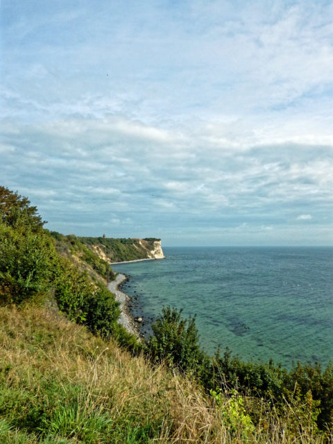 Bild: Blick vom Hochuferweg vom Fischerdorf Vitt zum Kap Arkona. Der alte Marinepeilturm des Jahres 1927 ist gut zu erkennen. Er diente zur Verbesserung der Sicherheit des Fährverkehrs auf der Königslinie zwischen Sassnitz und Trelleborg. Seine technischen Einrichtungen wurden 1945 nach dem Zweiten Weltkrieg zerstört. Klicken Sie auf das Bild um es zu vergrößern.