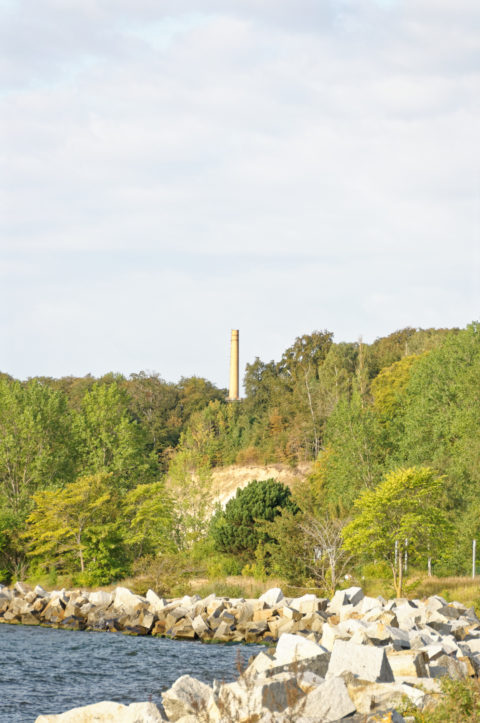 Bild: Schornstein des zentralen Heizkraftwerkes aus der Zeit des 18. Marinepionierbataillon der NVA auf dem ehemals militärisch genutzten Areal des Schlosses Dwasieden in der Nähe des Hafens von Sassnitz. Der Schornstein ist eine weithin sichtbare Landmarke. Blick vom Hafen von Sassnitz. Klicken Sie auf das Bild um es zu vergrößern.